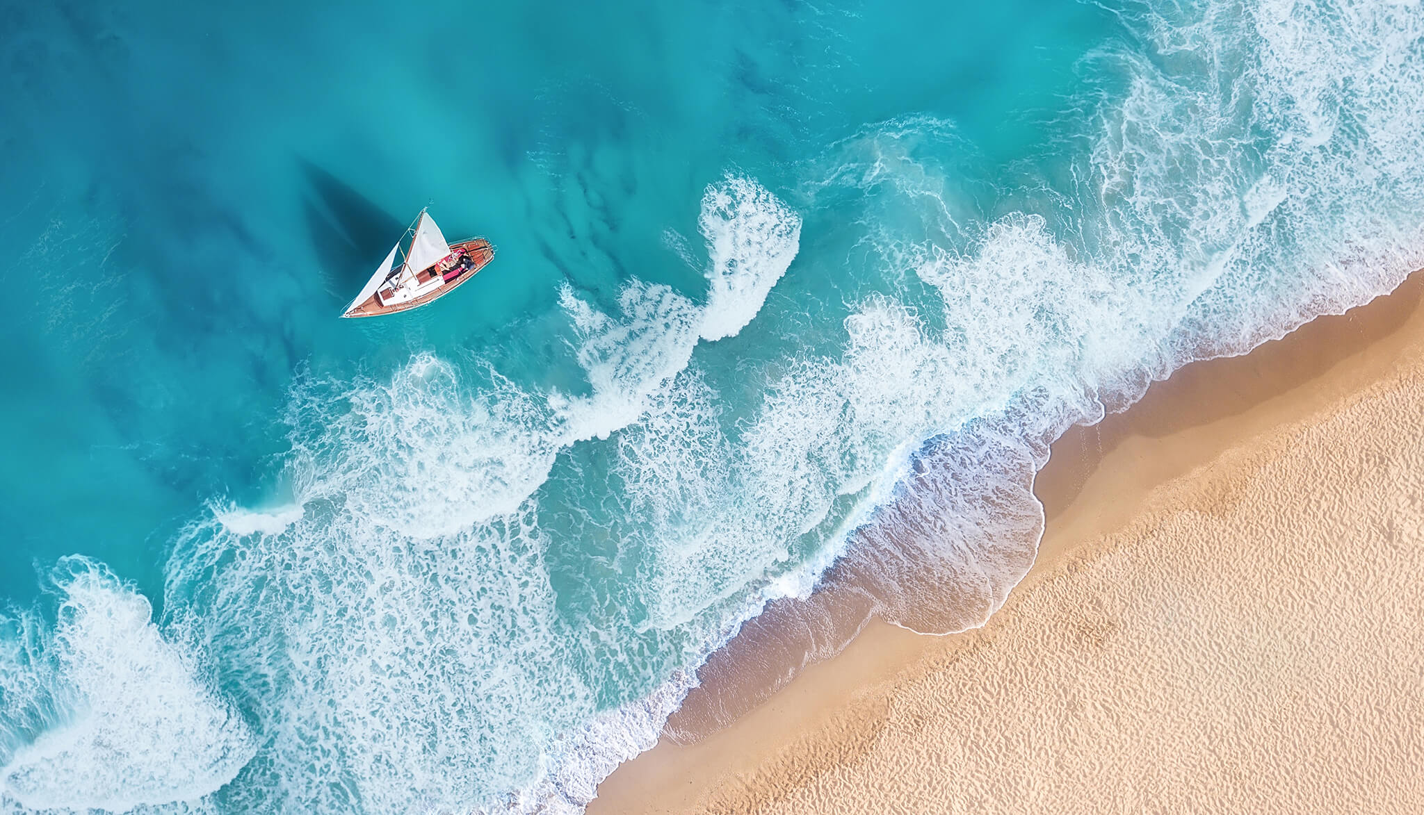 A sailboat glides just outside the waves of a Caribbean island.