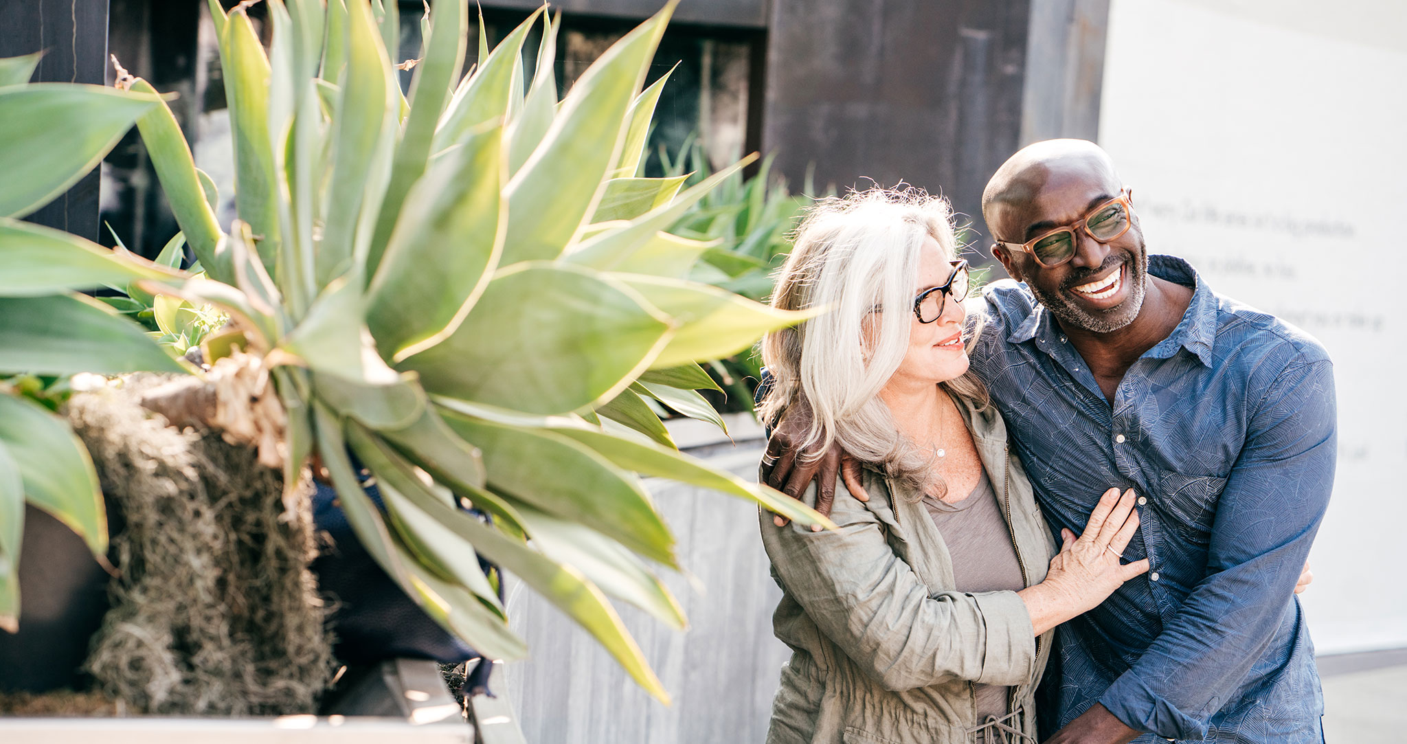 A happy couple walks outside, next to a wall with landscaping.