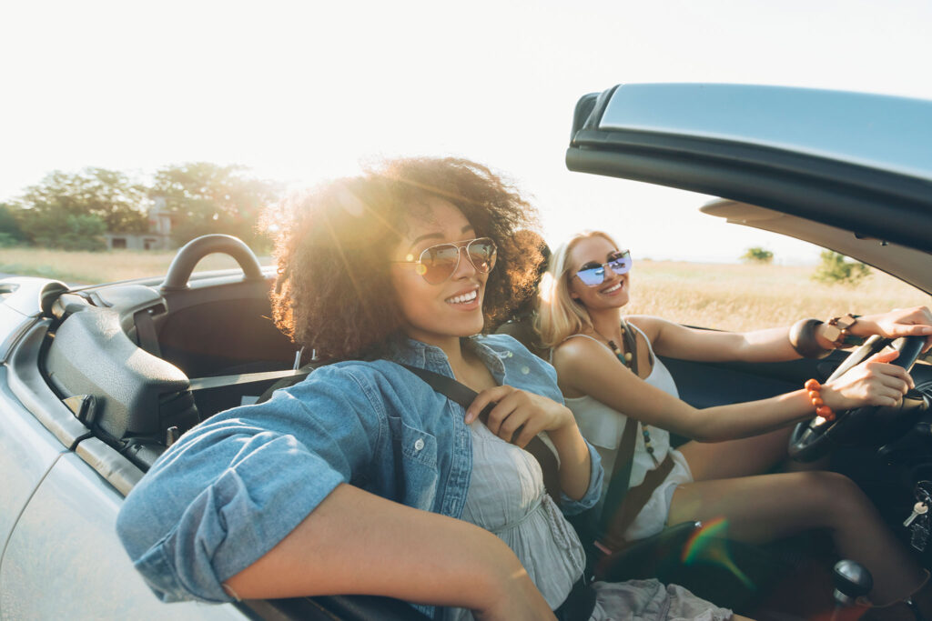 Two women seated in a convertible enjoy a sunny day.