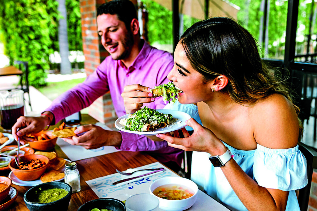 young latin woman eating mexican tacos on a restaurant terrace in Mexico Latin America, feeling happy on a summer day