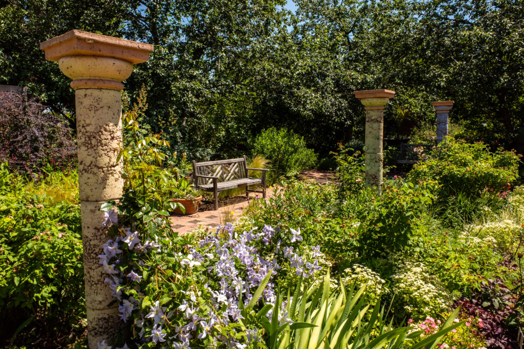 Sitting bench by pillars in lush greenery and flowers in Denver Botanic Gardens.