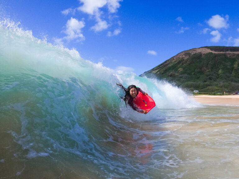 A young tanned Japanese woman happily riding a wave in Hawaii.